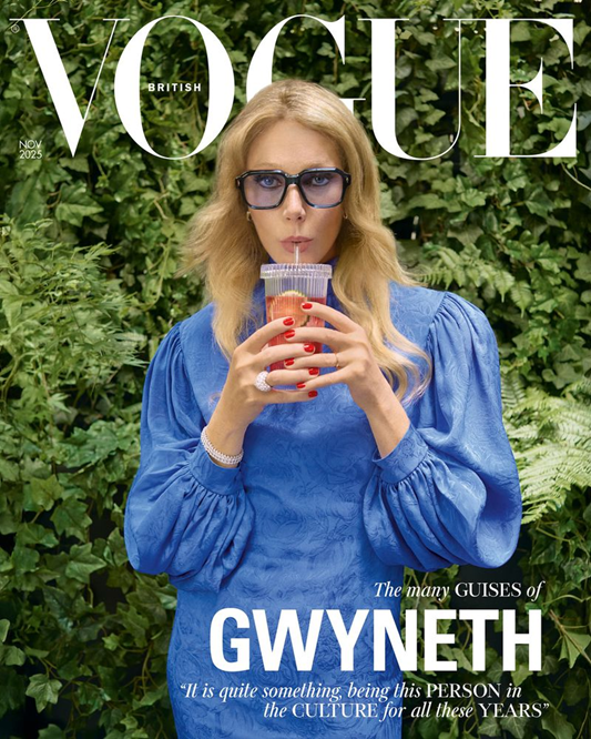 British Vogue November 2025 cover featuring actress Gwyneth Paltrow wearing a striking blue puffed-sleeve dress and dark-rimmed glasses, drinking from a straw, set against a backdrop of dense green foliage.